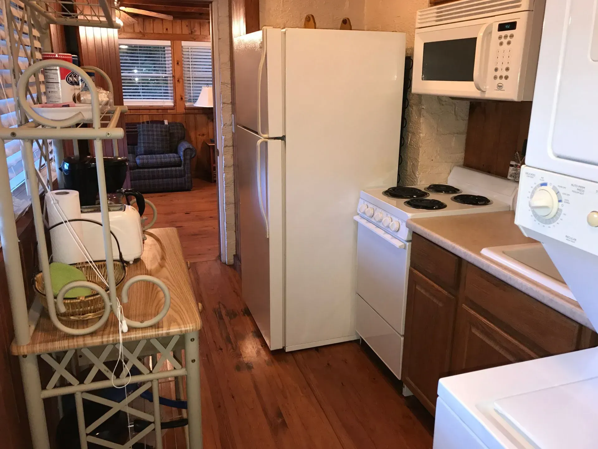Kitchen with a white refrigerator, stove, microwave, and a small sitting area with a blue armchair.