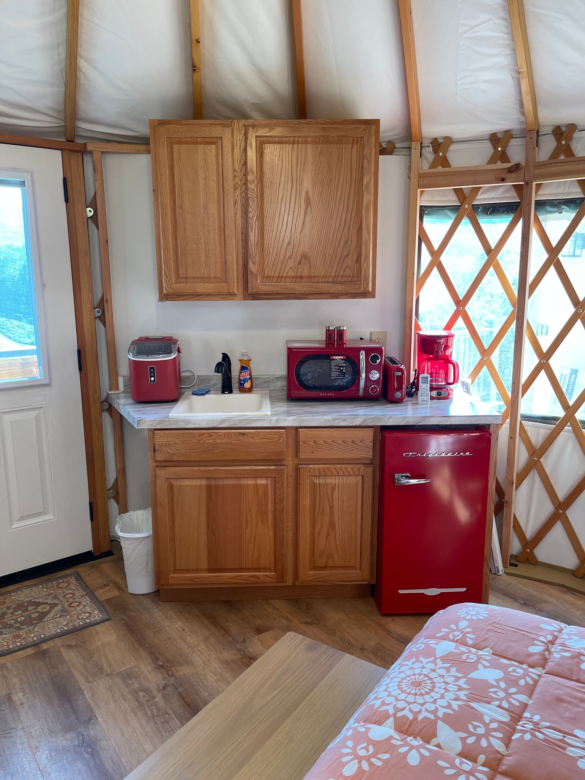 Interior of a yurt with a kitchen. Includes ceiling fan, cabinets, red appliances, and a door to the outdoors.