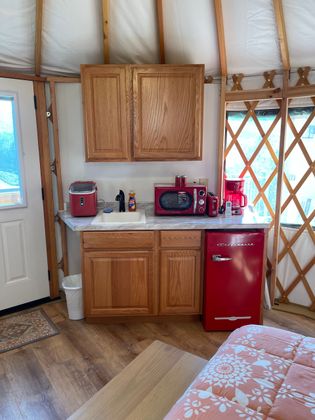 Interior of a yurt with a kitchenette, including a red microwave and fridge, cabinets, and a sink.