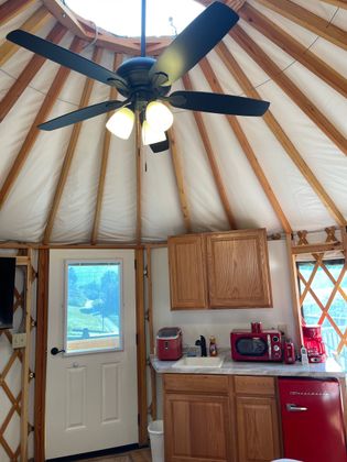 Interior of a yurt with a ceiling fan, skylight, and wooden cabinets.