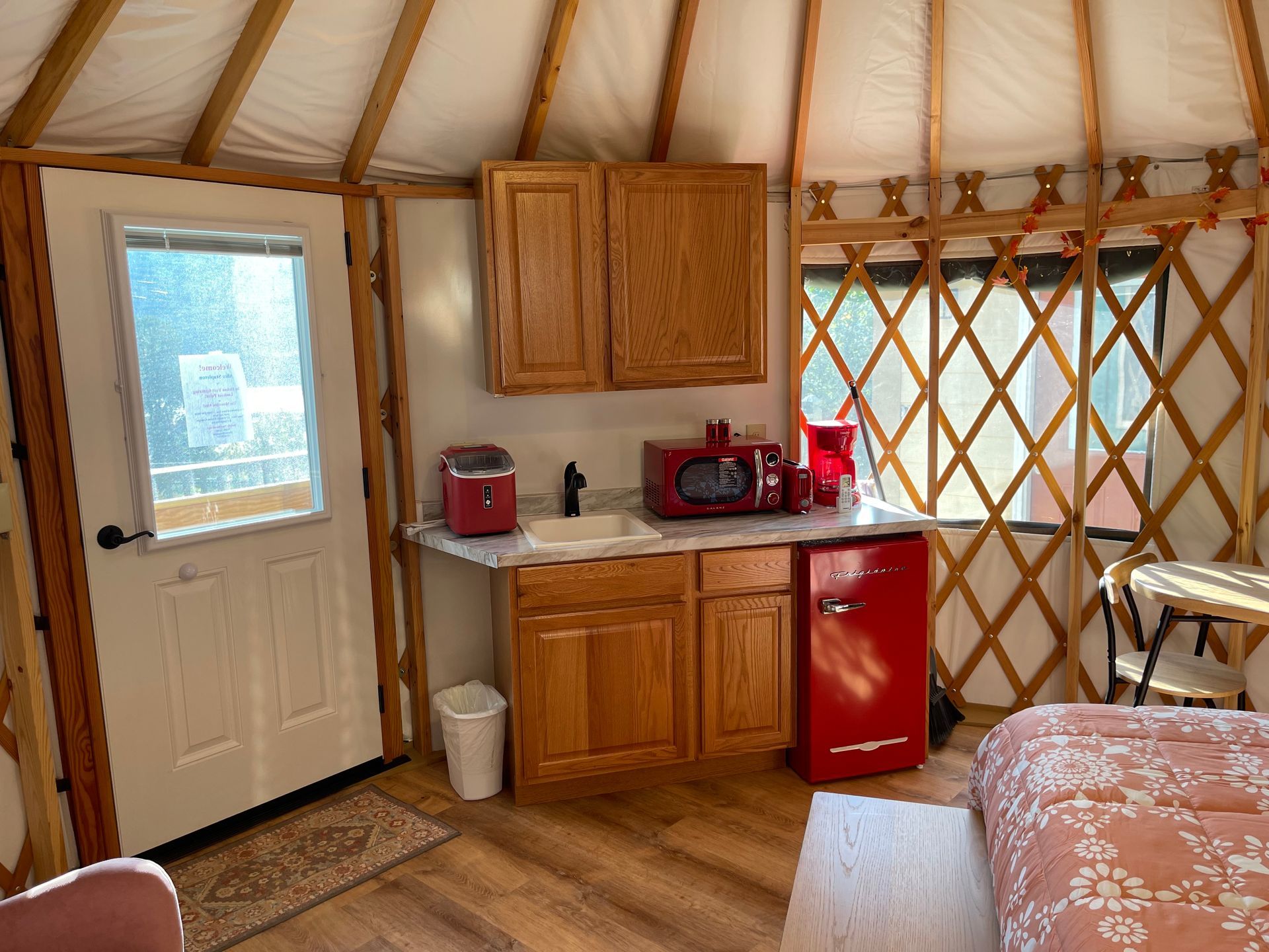 A yurt kitchen with red appliances, wooden cabinets, and a small sink.