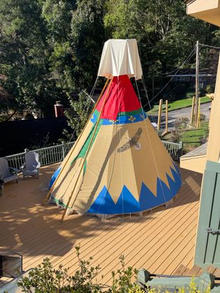 Tan tepee on a wooden deck, blue and green accents, red and white top.