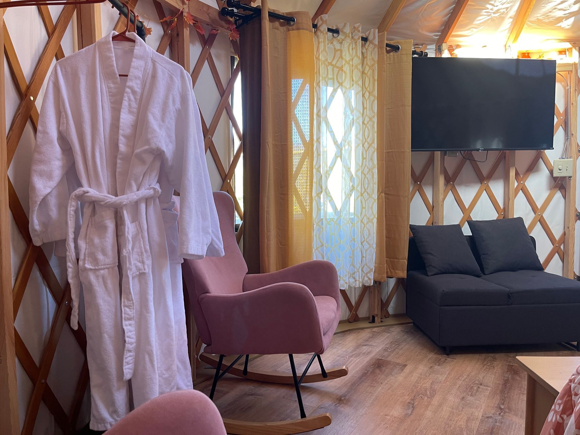 Interior of a yurt with two pink rocking chairs, TV, and wooden frame structure.