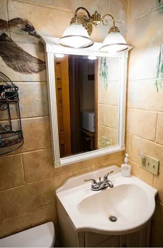 Bathroom sink with a mirror, light fixture, and patterned, tan-colored tile walls.