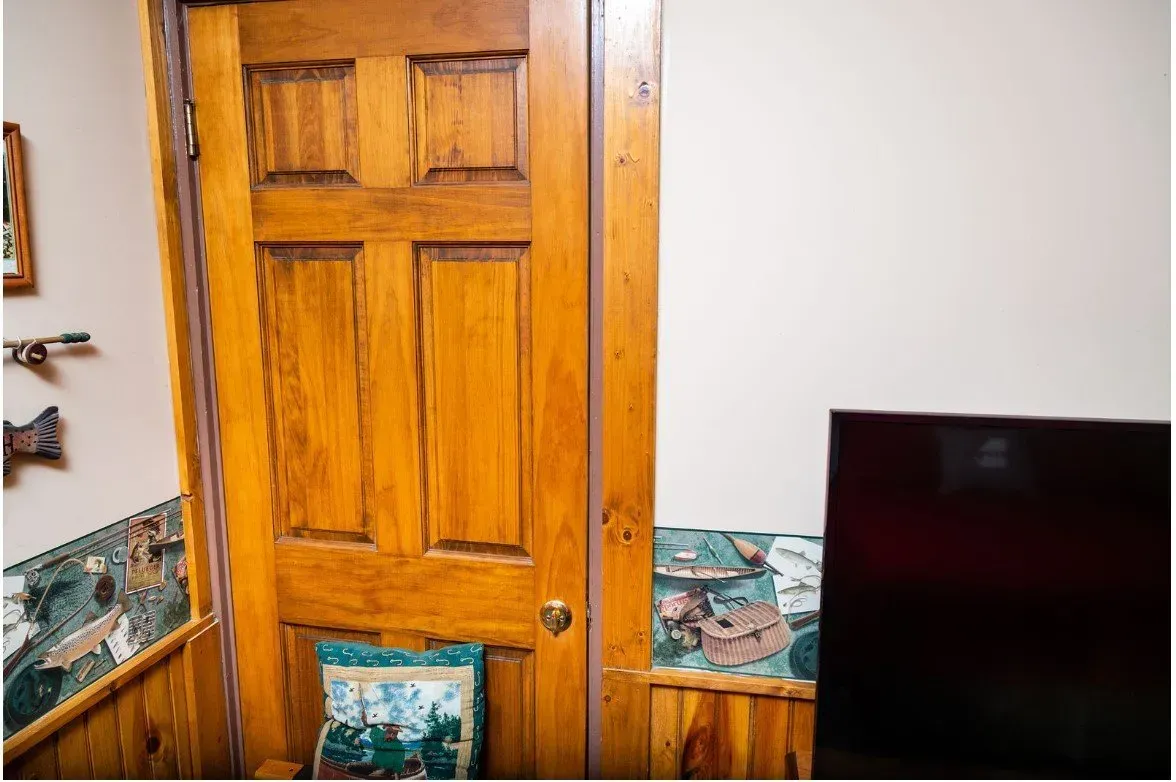 Wooden door in a room with paneled walls, wallpaper, and a dark electronic screen.