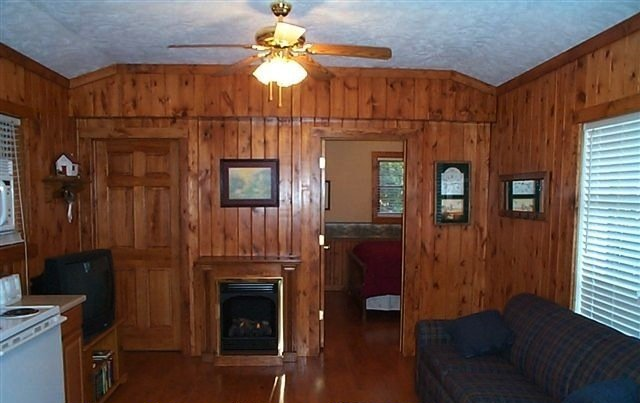 A cozy room with wood paneling, a fireplace, sofa, and a doorway leading to another room.