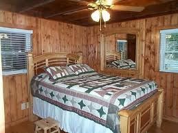 Bedroom with wooden walls, bed, quilt, mirror, windows, and small stool.