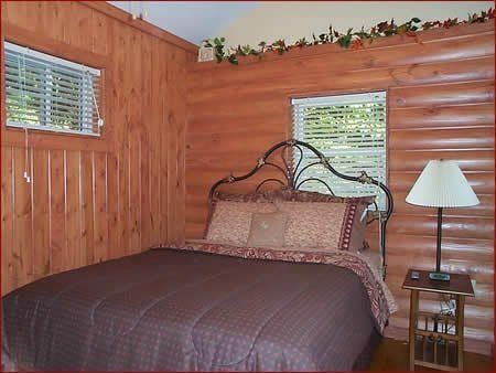 Bedroom with a bed, small window, and wooden walls.  Bedding is brown with decorative pillows and a lampshade.