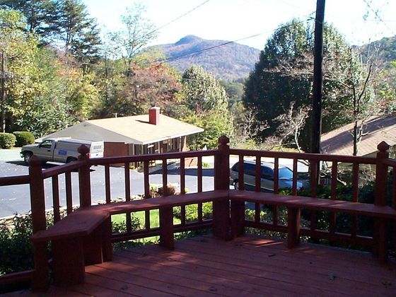 Wooden deck with a bench overlooking a building, trees, and a mountain.