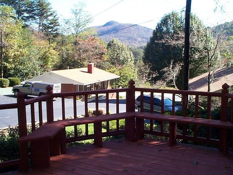 Wooden deck with a bench overlooking a building, trees, and a mountain.