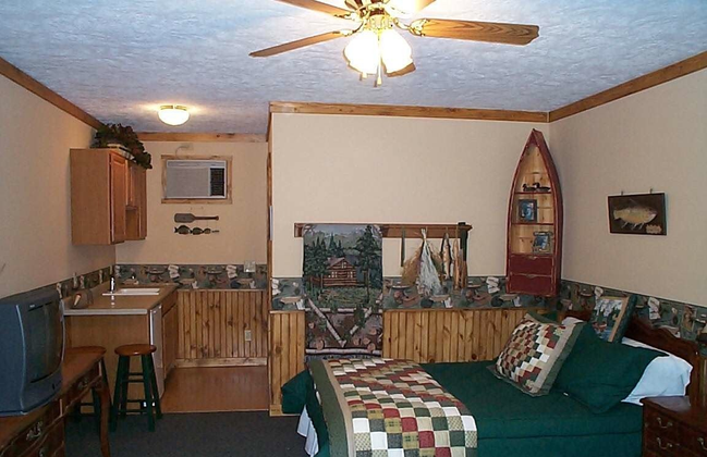 Cozy cabin-style motel room with a bed, TV, kitchenette, and decorative canoe bookshelf.