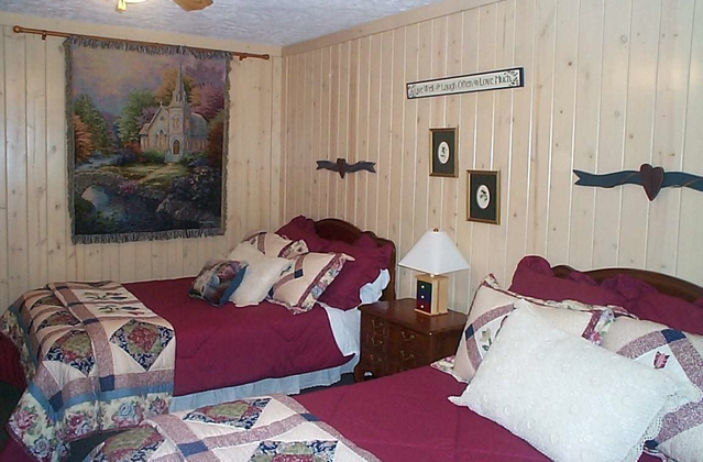 Two beds in a bedroom with burgundy bedding, wood-paneled walls, and a tapestry.