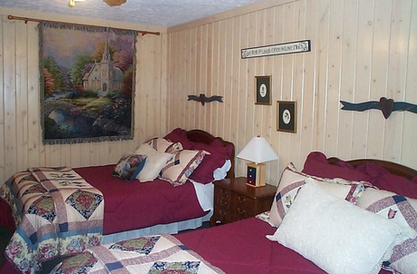 Two beds in a bedroom with burgundy bedding, wood-paneled walls, and a tapestry.