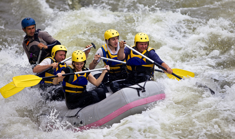 People rafting down a whitewater river, wearing helmets and life vests, splashing through rapids.