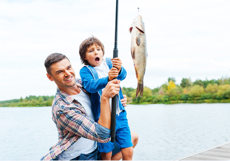 Father and son fishing; son with surprised expression holding fishing rod with caught fish.