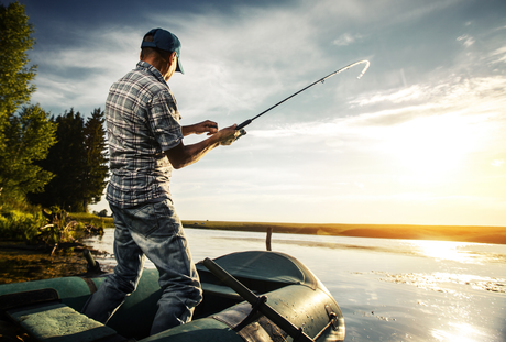Man fishing from a boat on a lake at sunset, holding a fishing rod with the sun shining.