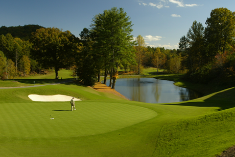 Golfer on green putting toward hole, lake and trees in the background.