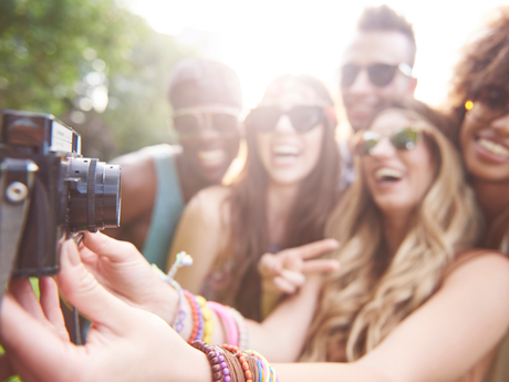Group of friends taking a selfie with a camera, laughing and smiling in the sun.