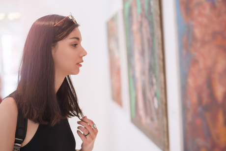 Woman in art gallery, gazing at colorful abstract paintings.
