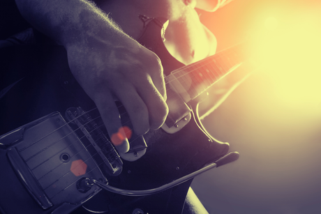 Person playing an electric guitar with hand on the strings, stage lighting in the background.