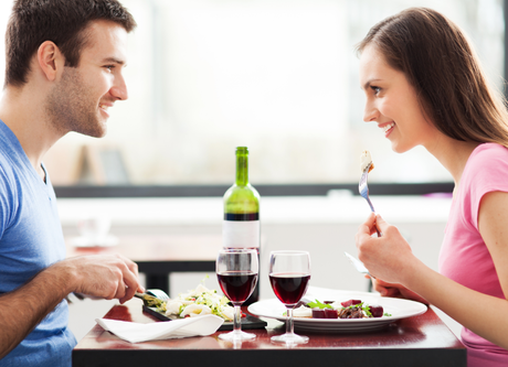 Couple smiling and eating dinner at a restaurant, red wine on the table.