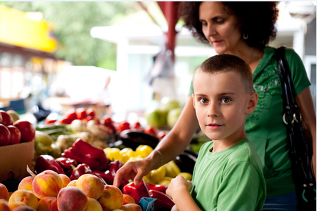 Woman and child at outdoor market selecting produce, with peaches in foreground.