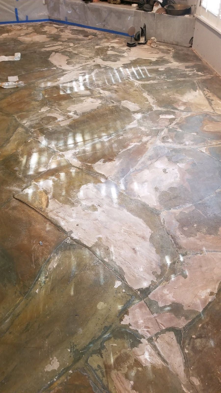 A worn, multi-colored floor with peeling sections; construction in progress, indoor setting.