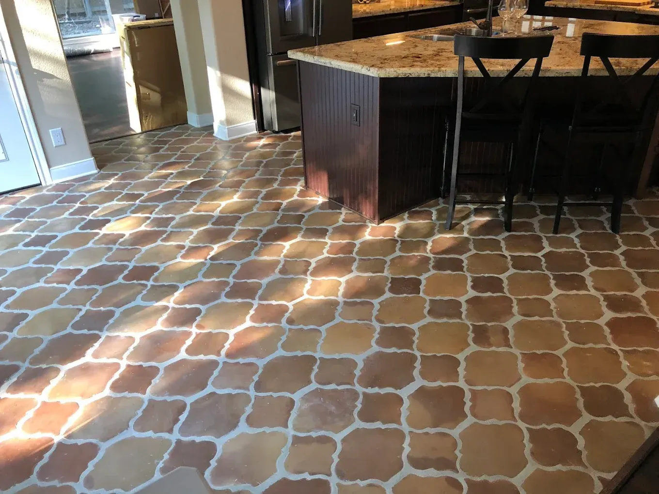 Terra cotta tile floor in a kitchen, with an island and stools in the background.
