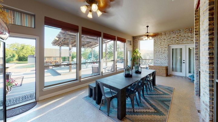 A dining area with a long dark table and metal chairs on a geometric rug, set in a sunlit room with brick walls.