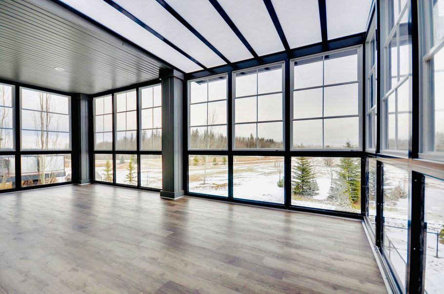 Sunroom with wood floors, large windows, and a glass ceiling looking out onto a snow-covered field with evergreen trees.