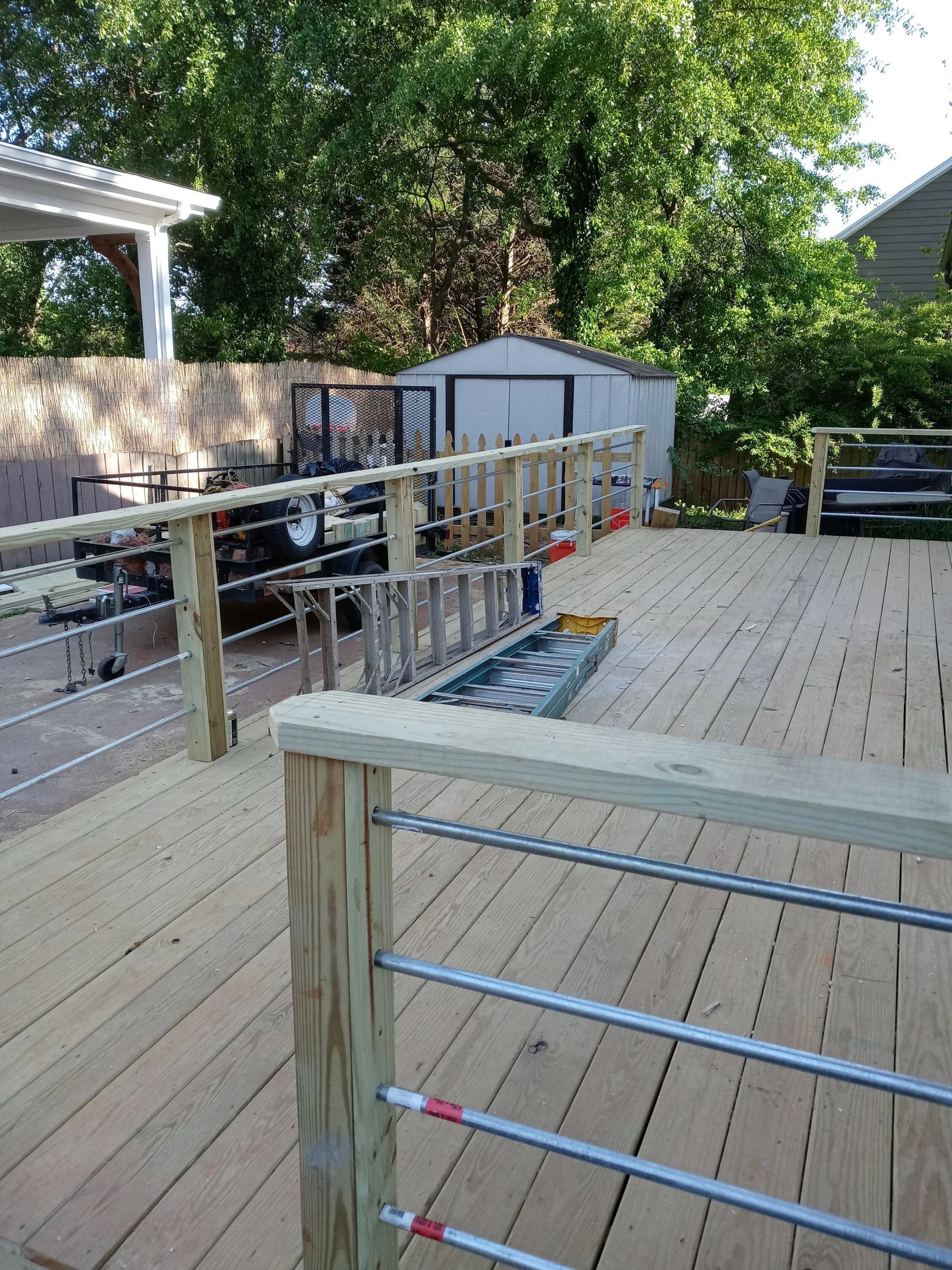 Wooden deck with cable railings and a ramp leading to a shed in a backyard.