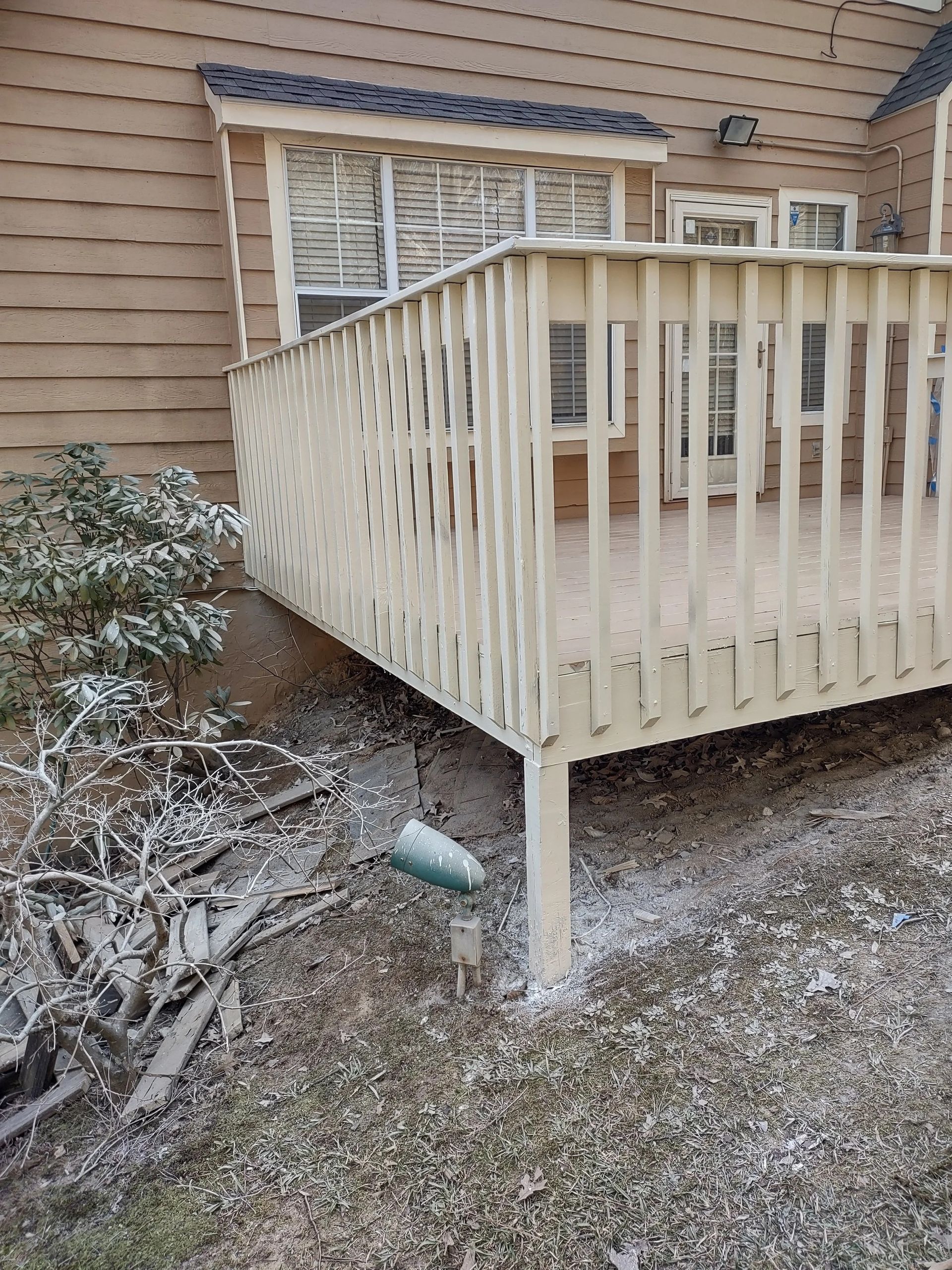 Wooden deck with beige railings, snow-covered ground, and a section of a house in the background.