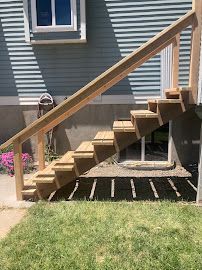 Wooden outdoor staircase with handrail beside a house, over a grassy yard.
