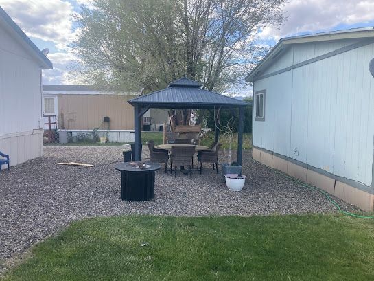 Backyard patio with a gazebo, table and chairs, gravel ground, lawn, and potted plants between two houses