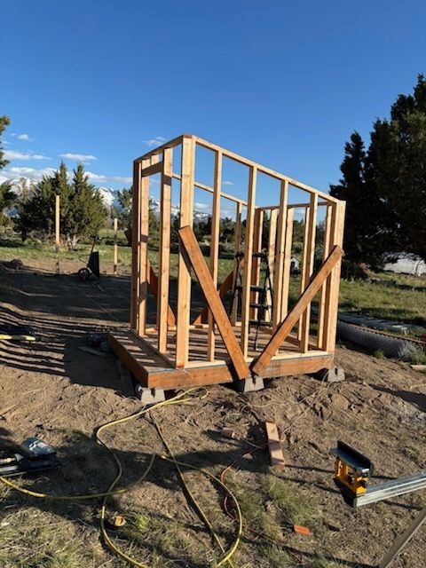 Wood-framed shed under construction on a dirt lot, with tools and materials nearby.