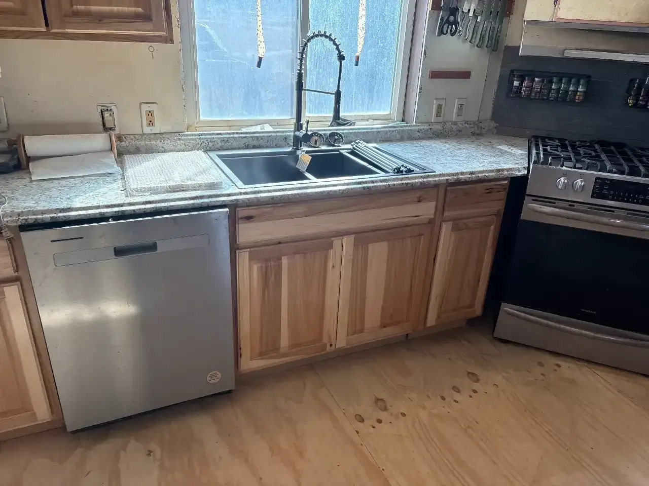 Kitchen with sink under a window, stainless dishwasher, wooden cabinets, and oven beside a granite countertop.