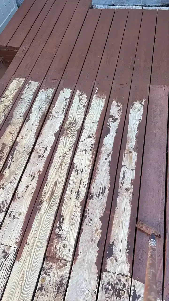 Weathered wooden deck boards with peeling white paint and a small metal bolt on the right side