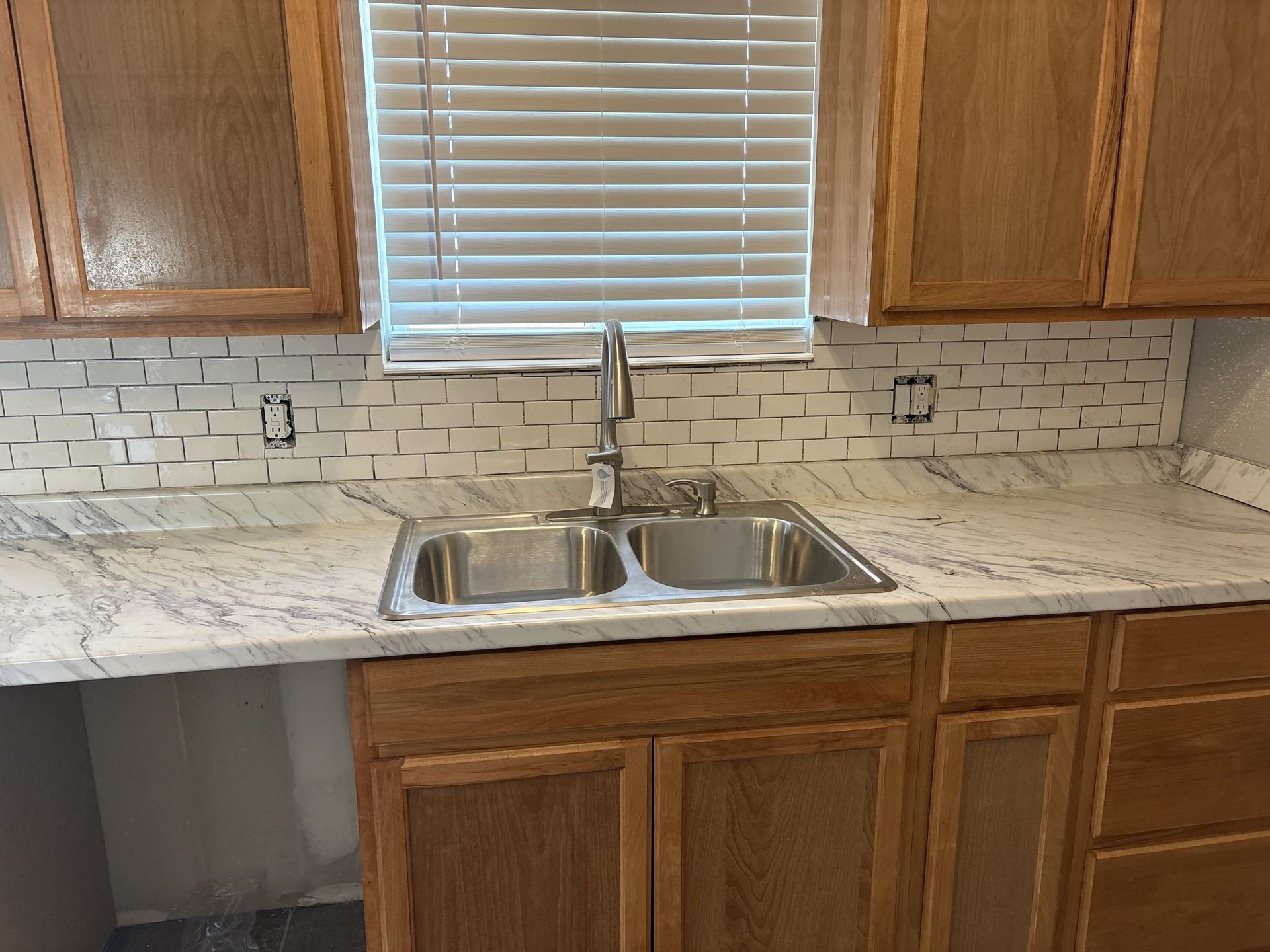 Kitchen sink under window with white tile backsplash and wooden cabinets