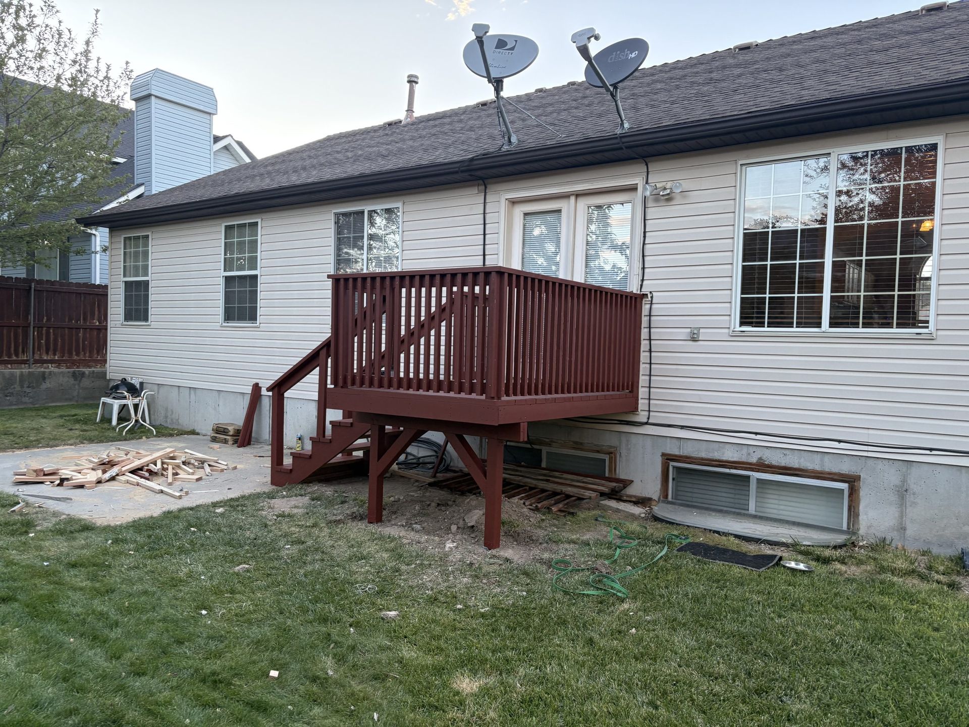 Backyard view of a house with a small wooden deck, windows, satellite dishes, and a lawn