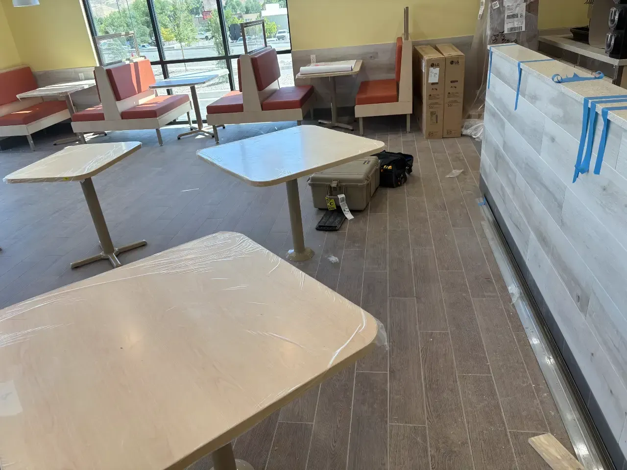 Bright café seating area with tables, red booths, large windows, and stacked boxes on the right