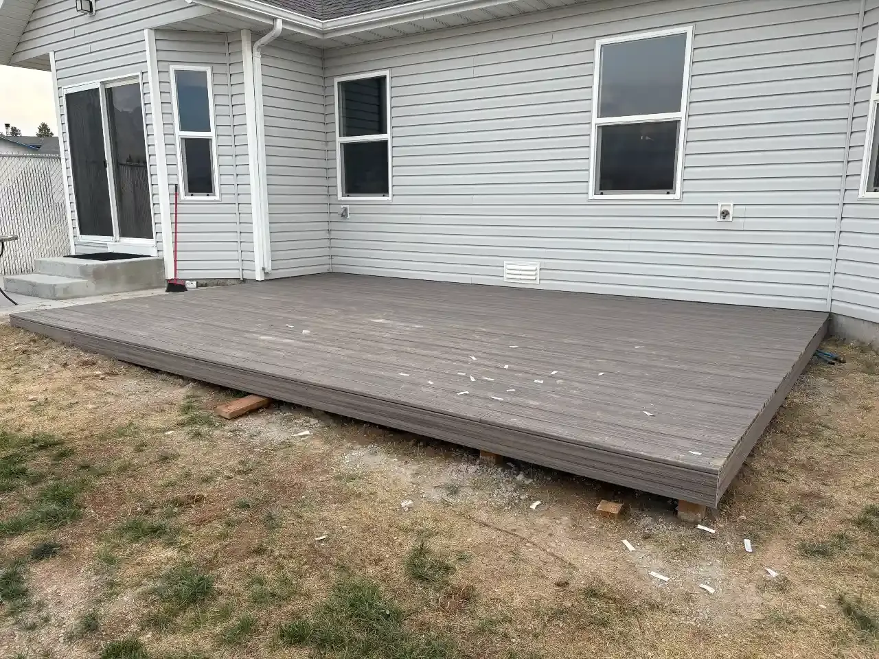 Gray wooden deck attached to a house exterior with white siding and a small ramp or steps at the left end