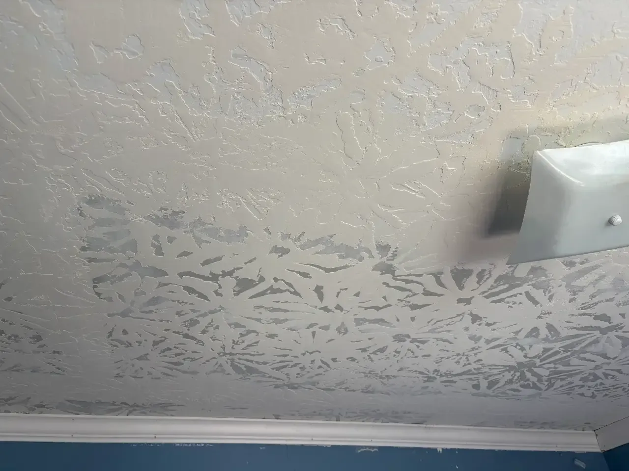 Ceiling with peeling paint and a white smoke detector near the corner.