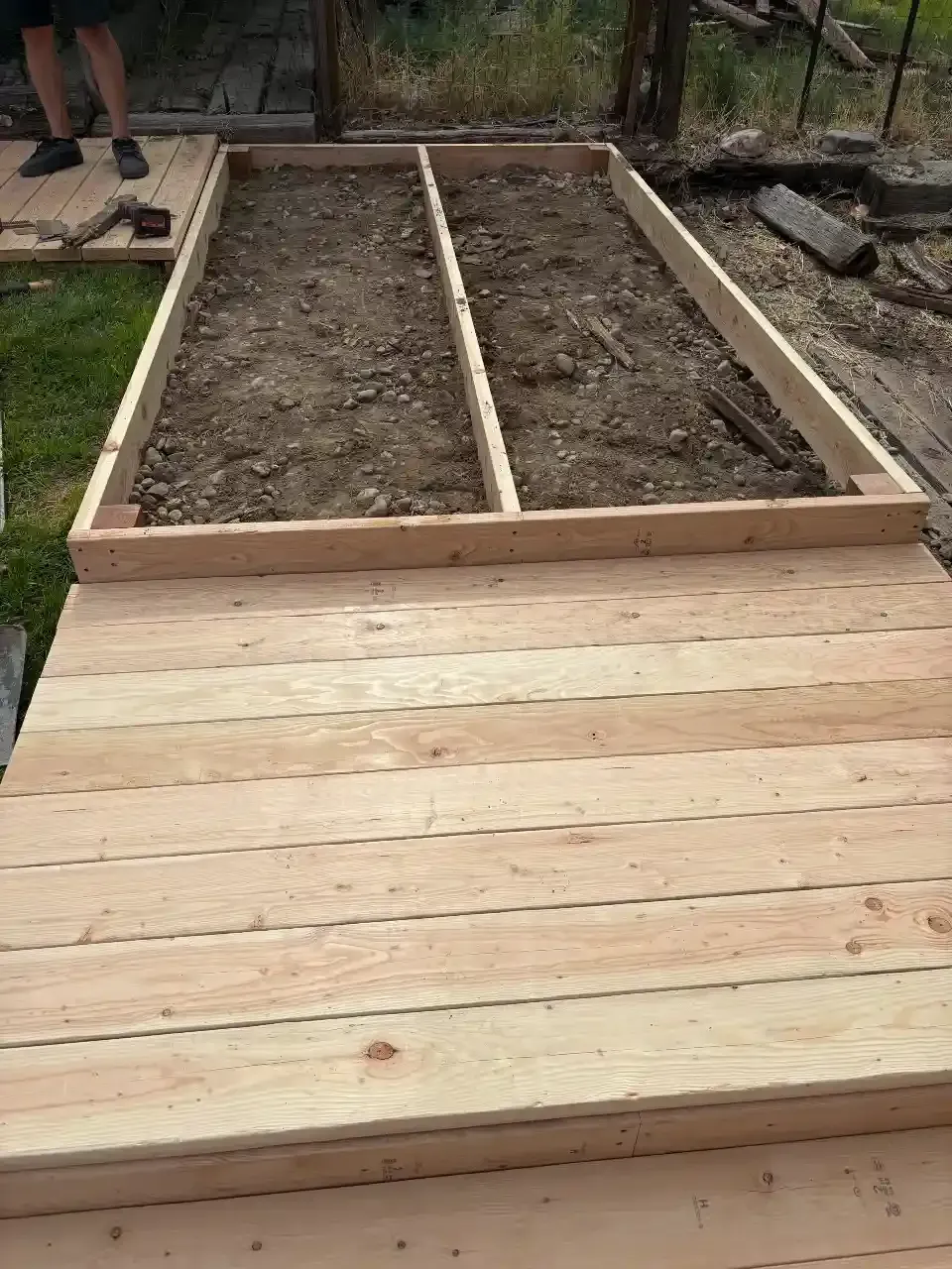 Wooden deck leading to a raised garden bed filled with soil and divided into sections.