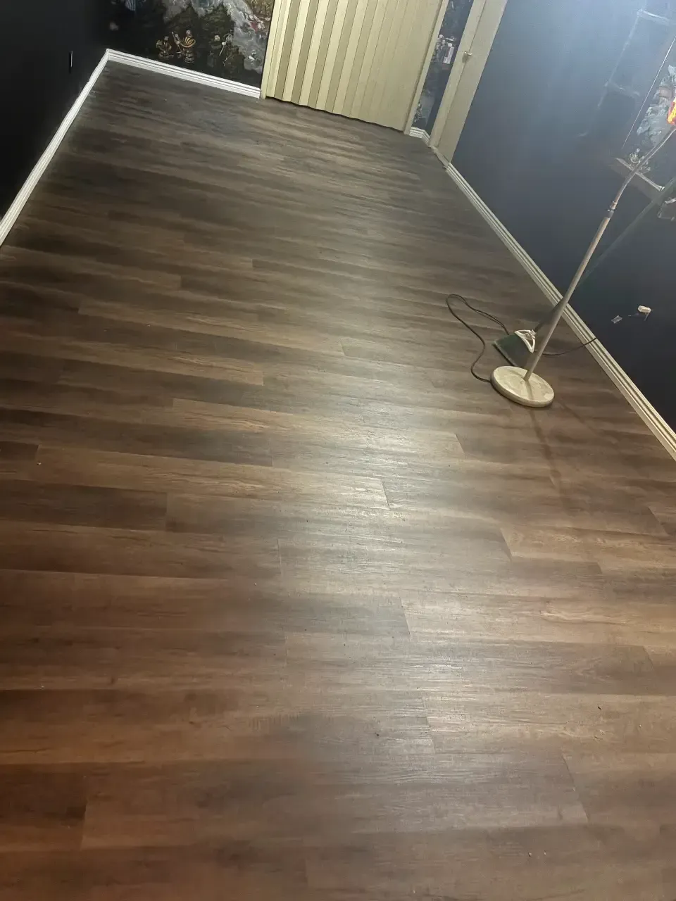 Empty room with dark wood floor, curtains, and a standing fan on the right.