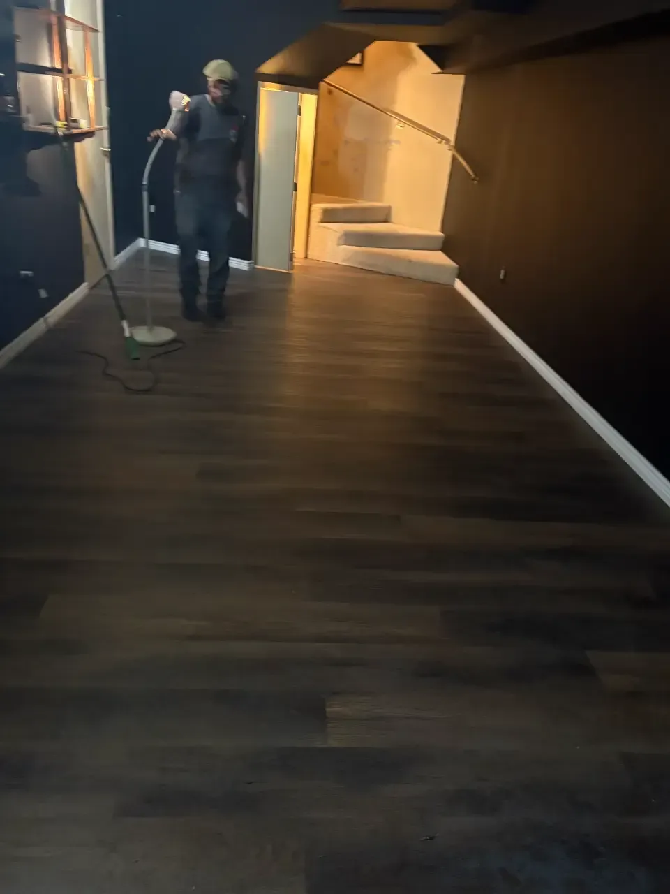 Person mopping a dark hallway with wood flooring and warm lighting near an open doorway