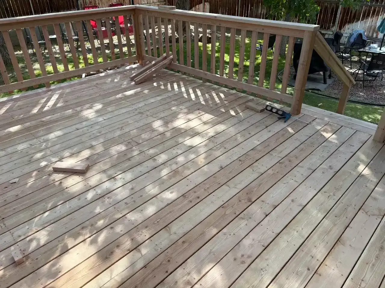 Wooden deck with railing, sunlit planks, and a view of greenery beyond.