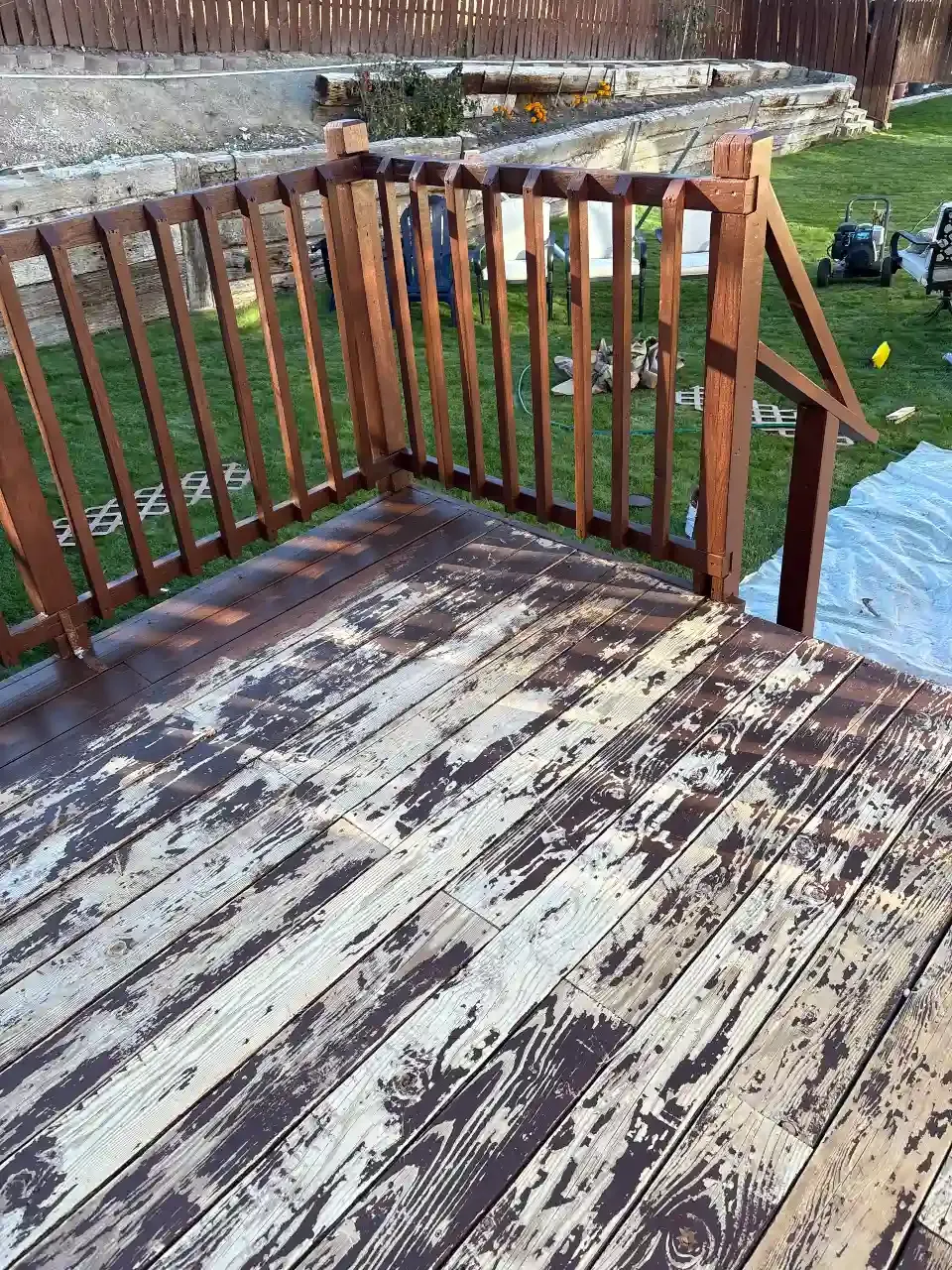 Weathered wooden deck with peeling white paint and a brown railing overlooking a grassy yard.