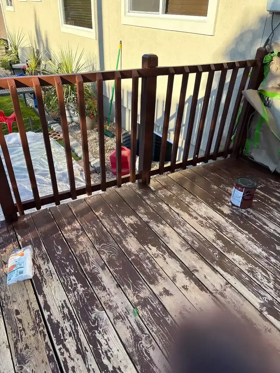 Weathered wooden porch with railing overlooking a yard, with a small red bucket near the fence.