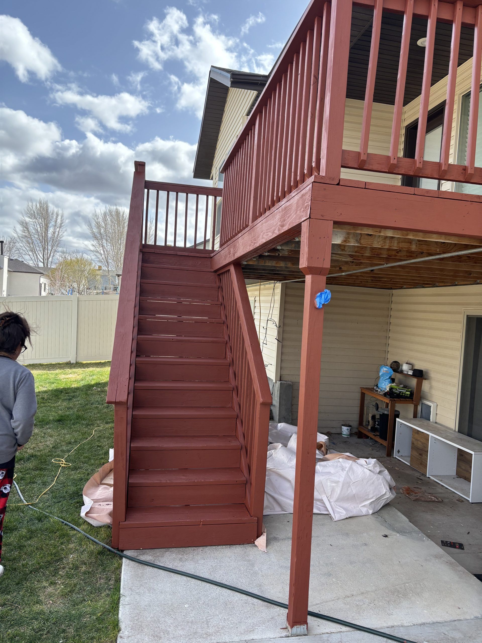 Red wooden exterior staircase leading to a raised deck beside a house, with a person partially visible at left.