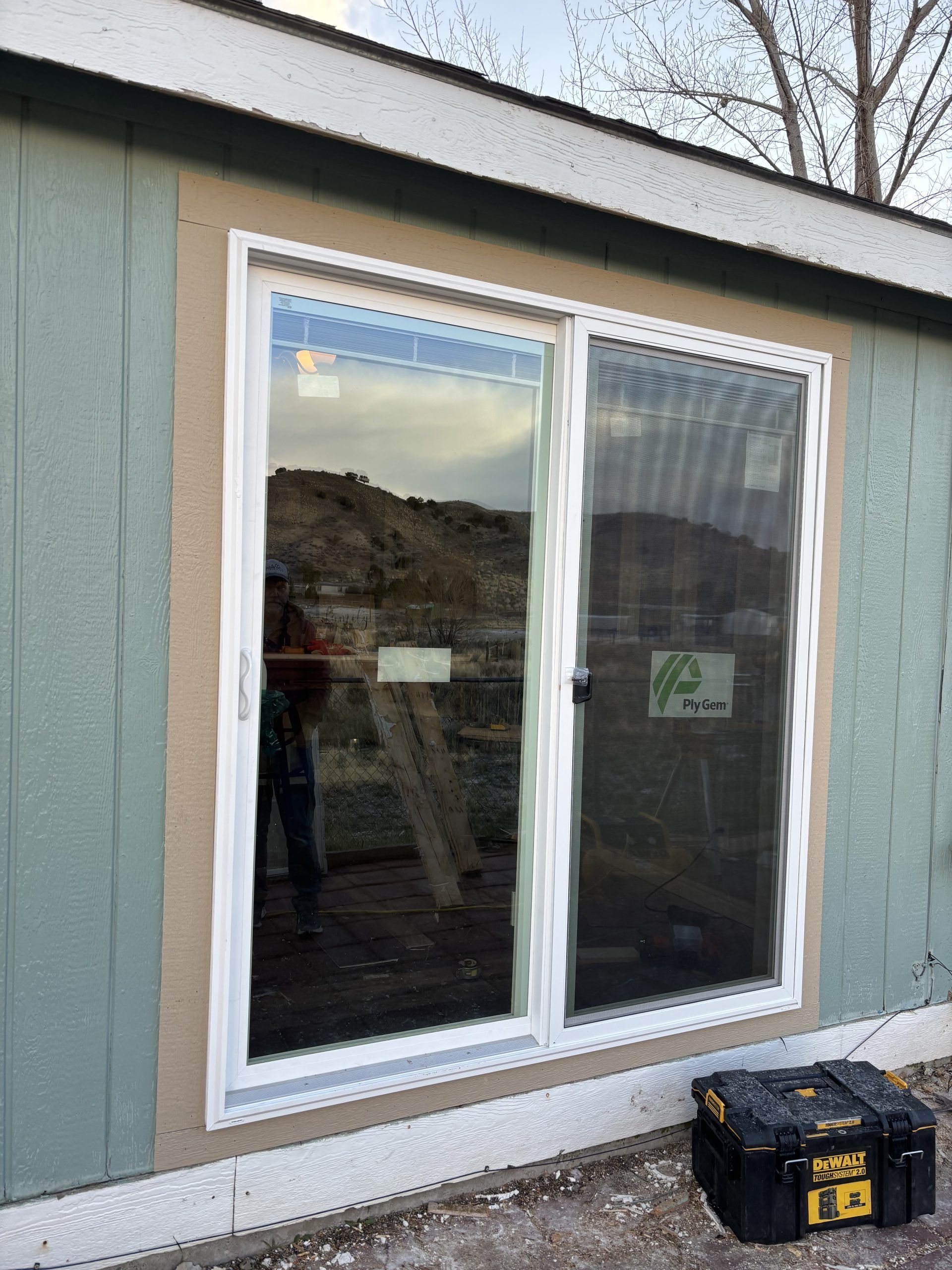 White-framed double window in a gray house wall, with a black toolbox on the ground below.
